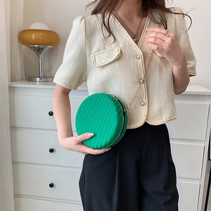 Détail du sac à bandoulière rond vert avec plis verticaux et chaîne dorée