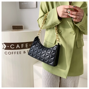 Detail of black quilted leather shoulder bag with chunky gold chain strap worn by model