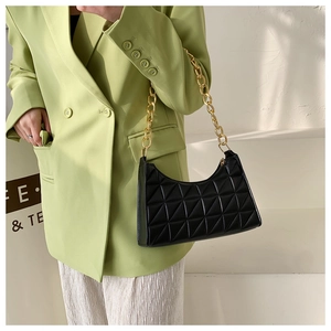 Detail of black quilted shoulder bag with chunky gold chain strap on model in suit