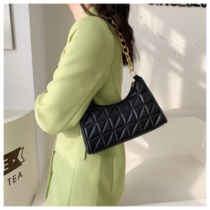 Detail of black quilted shoulder bag with chunky gold chain strap worn with green blazer