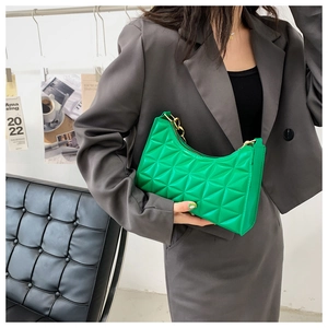 Detail of green quilted hobo bag with gold chain strap shown on a leather sofa