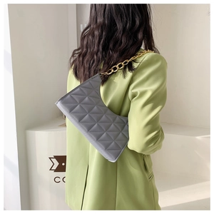 Close-up of a grey quilted crossbody bag with a chunky gold chain strap on a model