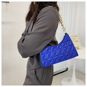 Quilted blue shoulder bag with gold chain strap shown on model in grey suit