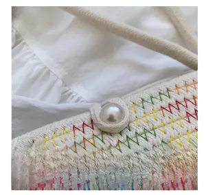Detail of hand-woven white bucket bag featuring rainbow stitching and a pearl button closure