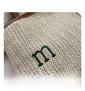 Detail of woven straw bag showing green embroidered letter m and brown leather trim