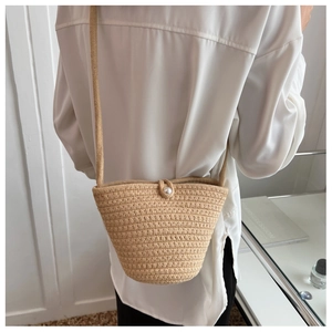 Detail of hand-woven straw bucket bag featuring a decorative pearl button closure