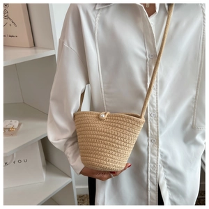 Detailed shot of beige woven bucket bag featuring an oversized pearl closure accent