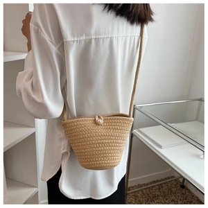 Detail of hand-woven straw bucket bag featuring a large pearl button and fine rope strap