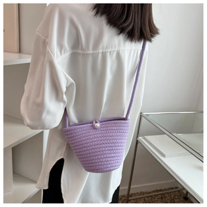 Close-up of a purple woven bucket bag with pearl buckle on a model from a side view