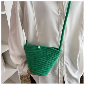 Detail of green hand-woven bucket bag with pearl button closure and woven shoulder strap