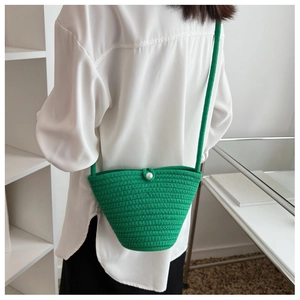 Detail of green hand-woven bucket bag featuring a white pearl button and woven strap