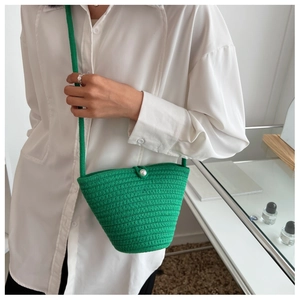 Close-up of green hand-woven bucket bag featuring a white pearl button and long strap