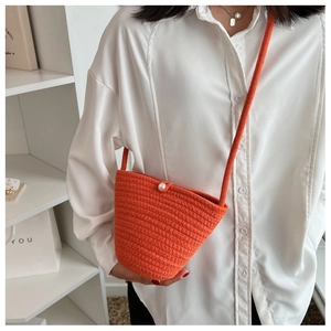 Close-up of bright orange woven bucket bag featuring a large pearl button and knit texture