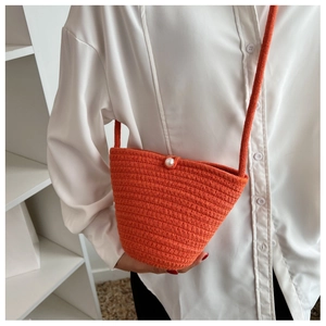 Detailed view of an orange woven bucket bag with a white pearl buckle and thin shoulder strap