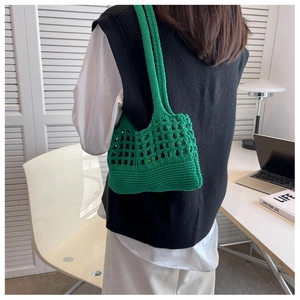 Borsa tote in maglia verde indossata a spalla da una modella in un ufficio stile moderno