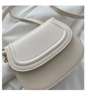 Close-up of cream semi-circle crossbody bag with unique textured edge and gold D-ring