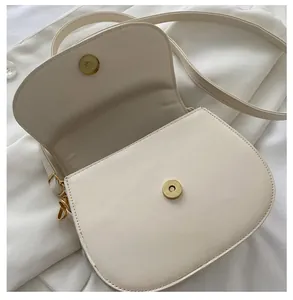 Detail of the durable magnetic metal clasp and creamy white leather texture on saddle bag