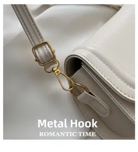 Detailed close-up of golden lobster clasp and leather texture on a beige shoulder bag