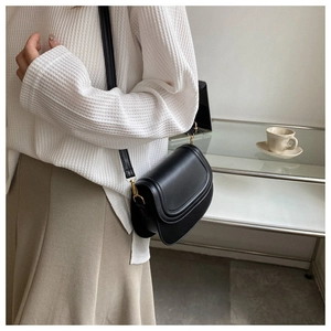 Detail of minimalist black saddle bag with gold metal buckle and adjustable strap