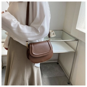 Side view detail of a vintage brown saddle crossbody bag with contrast piping and gold buckle