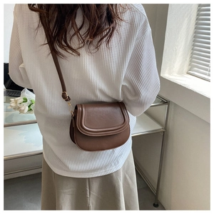 Brown saddle bag shown on shoulder in a minimalist and retro interior setting