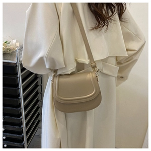 Detailed view of beige saddle bag with adjustable strap and gold buckle on a trench coat