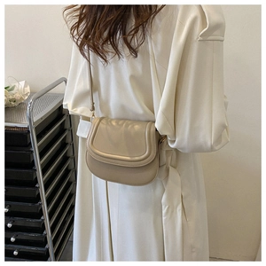 Detail view of a beige leather saddle bag with flap closure and delicate shoulder strap