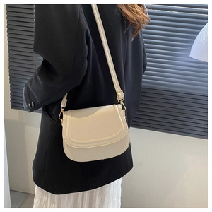 Model wearing a cream faux leather saddle bag with gold hardware and stitching detail