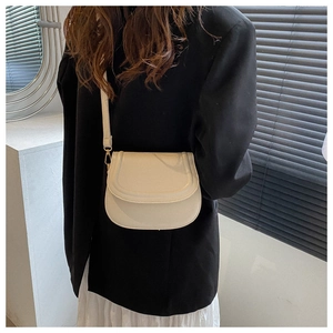 Close-up of off-white vintage saddle bag with adjustable strap on black blazer