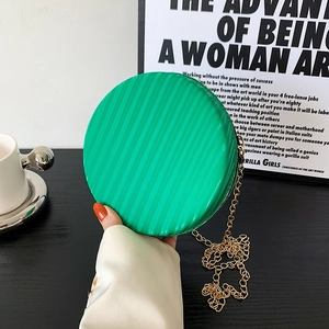 Sac rond vert moderne à chaîne avec rayures verticales tenu à la main dans un style chic
