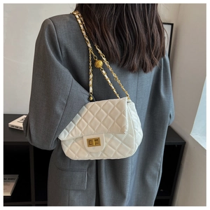 Detailed view of quilted white shoulder bag with gold ball chain and leather strap