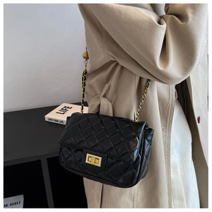 Detail of black quilted leather shoulder bag with gold chain strap on beige trench coat