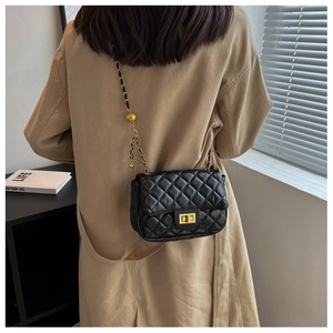 Close-up of black quilted shoulder bag with gold chain strap worn over a beige trench coat
