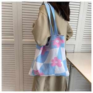 Macro detail of knit tote bag featuring blue checkerboard pattern and pink flower accents