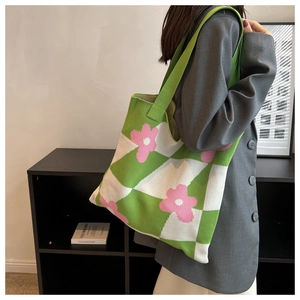 Detail of green and beige checkered knit tote bag with pink flowers worn over shoulder