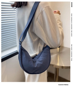 Dark blue nylon crescent crossbody bag with adjustable strap worn by a model indoors