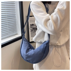 Blue nylon crescent moon crossbody bag worn by a model in a casual indoor setting