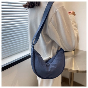 Detailed side view of a navy crescent nylon crossbody bag worn on a model in a minimal room