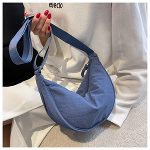 Close-up of the blue crescent shoulder bag featuring a smooth nylon texture and zip closure