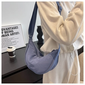 Blue nylon crescent bag worn crossbody by model in a minimalist modern room setting