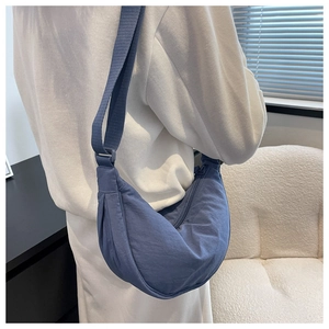 Side view of a blue nylon crescent bag worn crossbody by a model in a minimalist setting