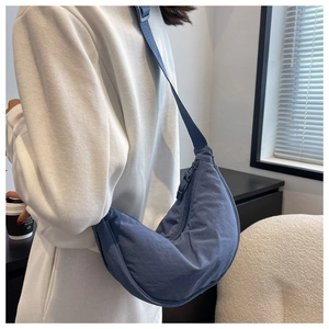 Blue nylon crescent shoulder bag shown on a model in a minimalist indoor setting