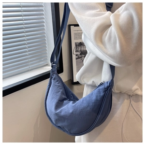 Blue nylon half-moon crossbody bag shown on shoulder with adjustable strap and casual style