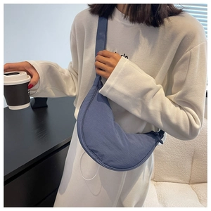 Blue nylon half-moon crossbody bag shown in a casual lifestyle setting with a model