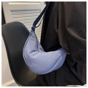 Blue crescent moon crossbody bag in durable nylon fabric worn by model from side view