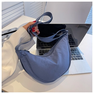 Detailed view of a blue nylon half-moon crossbody bag on a modern office desk
