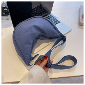 Close-up of blue nylon crescent bag with adjustable strap and laptop in the background