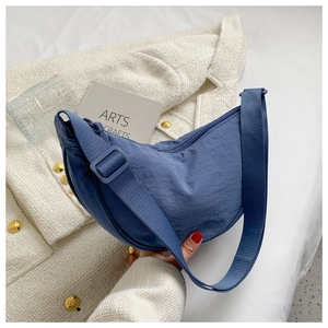 Flat lay of a blue crescent nylon crossbody bag on a textured coat with artistic decor