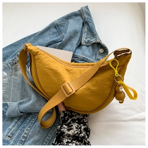 Detail of yellow nylon crescent cross-body bag featuring a cute bear keychain on denim