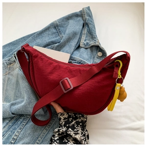 Detail of burgundy crescent nylon shoulder bag with adjustable strap and yellow bear charm